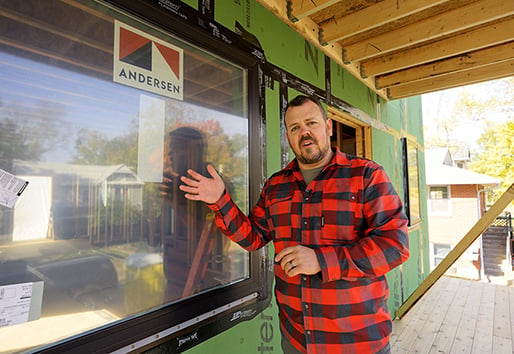 A man stands next to an Andersen® window that has been installed in an under-construction home.