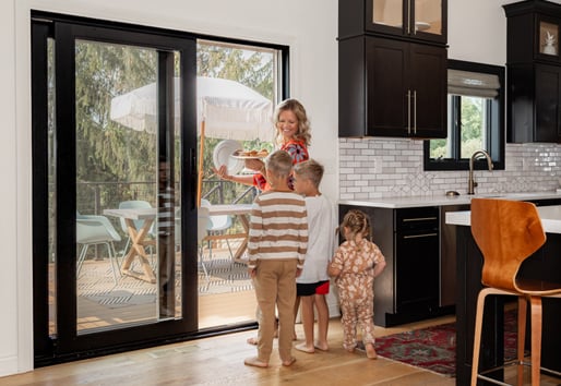 A family smiling in a kitchen next to a black sliding glass patio door. 