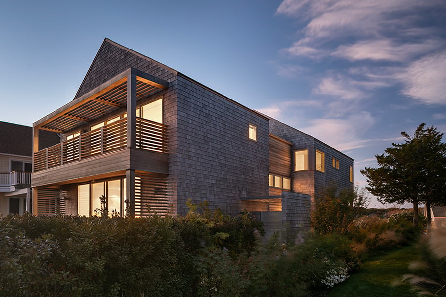 A two-story house with porches on each level and cedar shingles at dusk. 